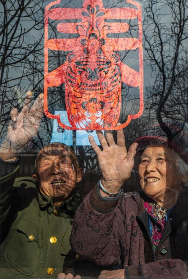 臘月里，霍州市師莊鄉(xiāng)馮南垣村村民師榮光(左)在災(zāi)后重建的新家里貼窗花。(霍州市委宣傳部供圖)