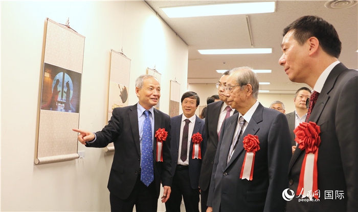 “湖州印象”攝影展主創(chuàng)、世界華人攝影協(xié)會副會長馮學(xué)敏向吳江浩大使、福田康夫前首相等嘉賓介紹展出作品。（人民網(wǎng) 許可攝）