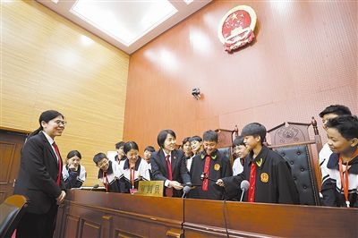 圖③：同學(xué)們穿法袍、敲法槌，爭(zhēng)做“小法官”。