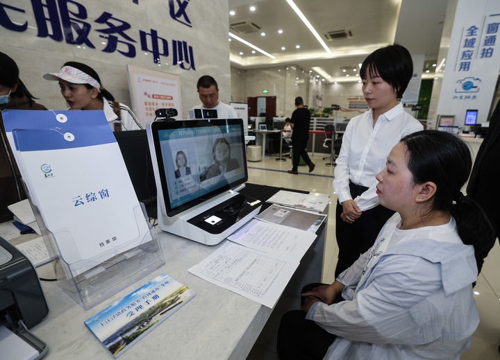 在浙江省嘉興市秀洲區(qū)王江涇鎮(zhèn)便民服務(wù)中心的“跨域通辦·云綜窗”窗口，辦理開(kāi)業(yè)登記的個(gè)體工商戶(hù)（右一）通過(guò)該系統(tǒng)與江蘇省蘇州市吳江區(qū)盛澤鎮(zhèn)行政審批局工作人員視頻連線(xiàn)，進(jìn)行身份讀取及材料線(xiàn)上審核（2024年5月9日攝）。新華社記者 徐昱 攝