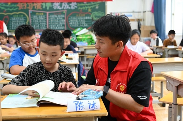 鄭州市二七區(qū)暑托班的志愿者輔導(dǎo)孩子寫作業(yè)。人民網(wǎng)記者王玉興攝